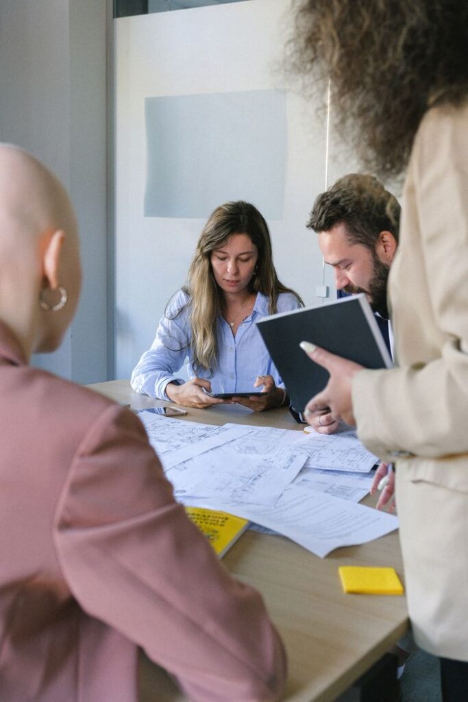 Young colleagues using tablet and talking at table with important documents in business office